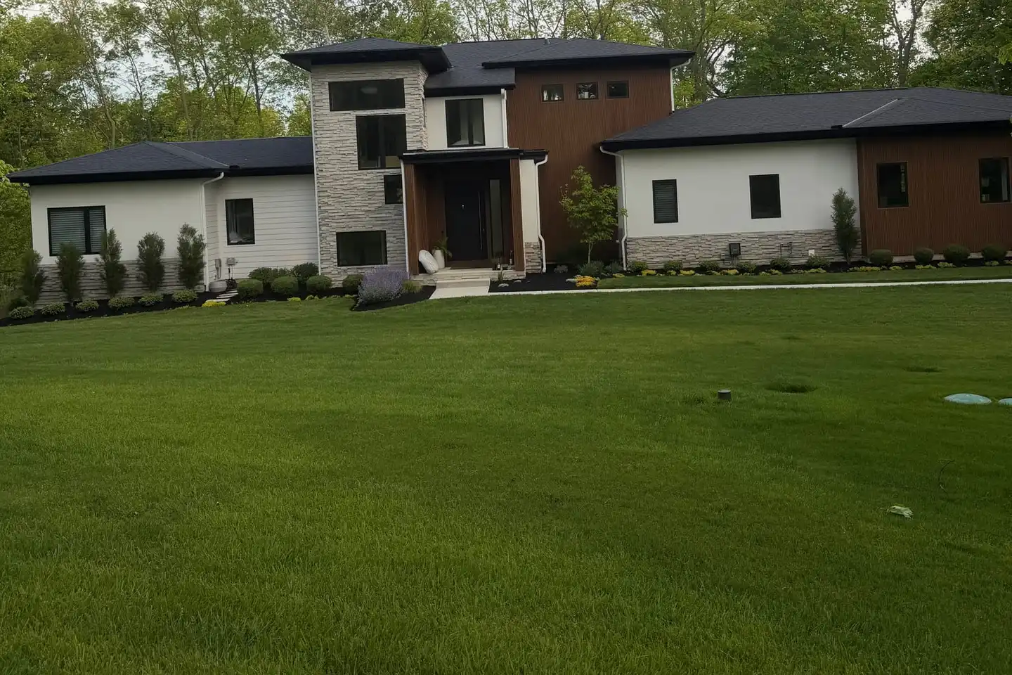 Newly established sod lawn sweeping up to a modern white and wood-clad home with fresh foundation planting beds
